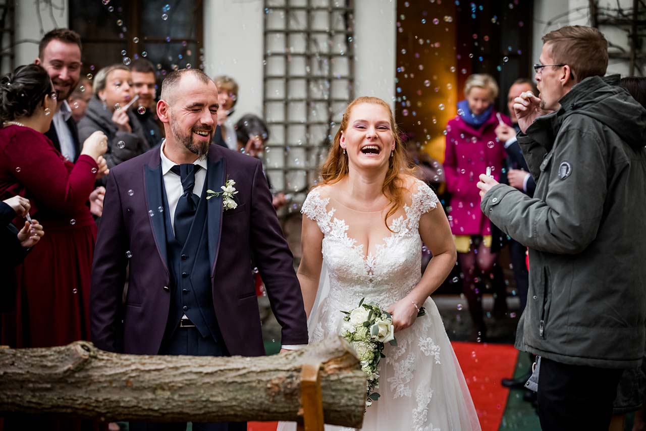 Brautpaar lächt herzlich - im Vordergrund Baumstamm zum sägen - Hochzeitsfotograf